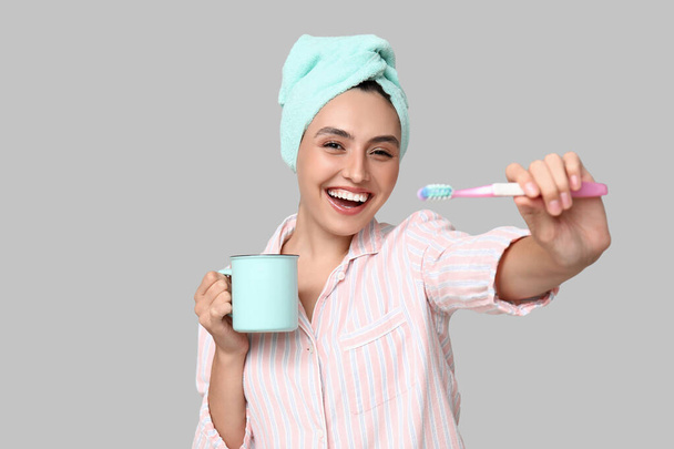 Junge Frau mit Zahnbürste und Tasse auf hellem Hintergrund - Foto, Bild