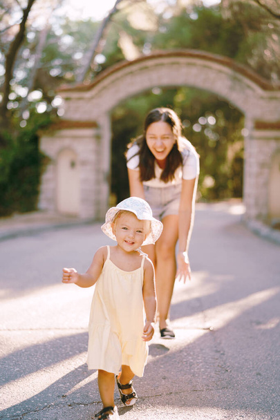 Riendo mamá persiguiendo a una niña por el camino en el parque. Foto de alta calidad - Foto, Imagen