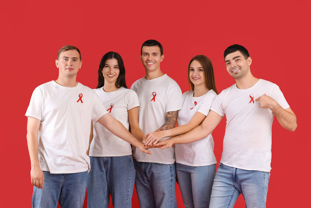 Kırmızı kurdeleli bir grup genç, renk arka planında el ele tutuşuyorlar. Dünya AIDS Günü konsepti - Fotoğraf, Görsel