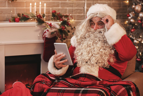Санта-Клаус с планшетным компьютером дома в канун Рождества - Фото, изображение