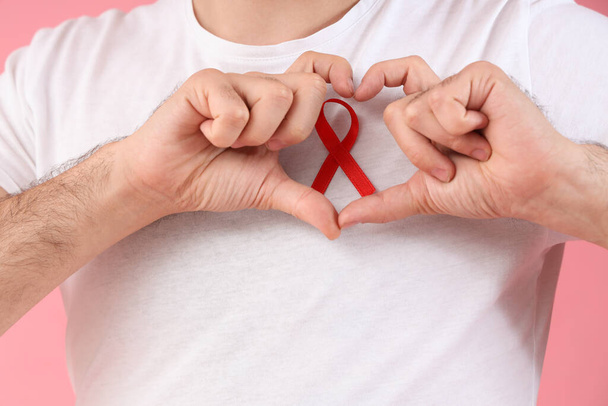 Young man with red ribbon making heart on pink background, closeup. World AIDS day concept - Photo, Image