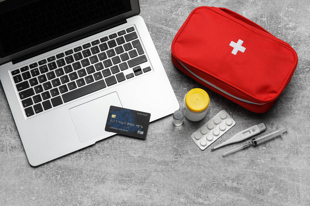 Φορητός υπολογιστής, πιστωτική κάρτα και κουτί πρώτων βοηθειών σε γκρι φόντο grunge - Φωτογραφία, εικόνα