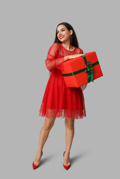 Красива молода жінка з різдвяним подарунком на сірому фоні - Фото, зображення
