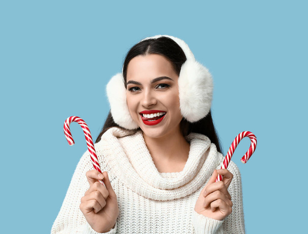 Hermosa mujer joven con bastones de caramelo de Navidad sobre fondo azul - Foto, imagen