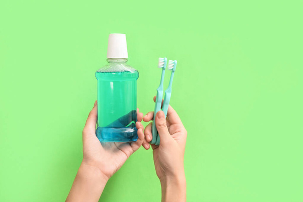 Γυναικεία χέρια με στοματικό ξέπλυμα και οδοντόβουρτσες σε πράσινο φόντο. - Φωτογραφία, εικόνα