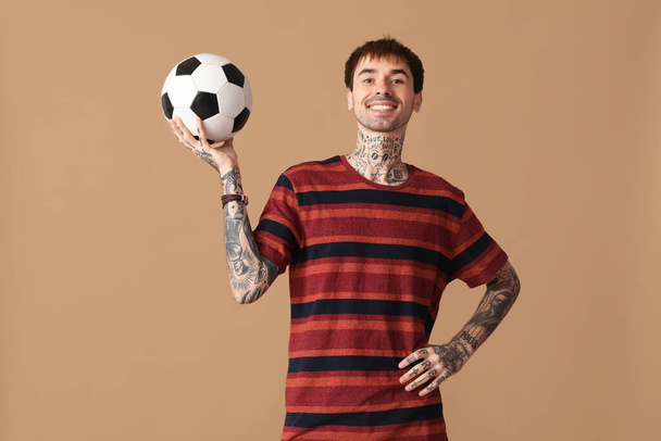 Feliz joven con pelota de fútbol sobre fondo marrón - Foto, imagen