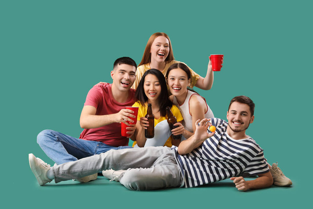 Group of young friends with beer and ball on green background - Photo, Image