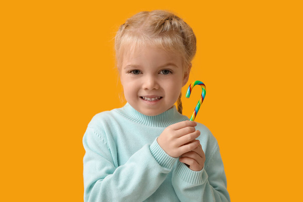 Cute little girl with colorful candy cane on yellow background - Photo, Image