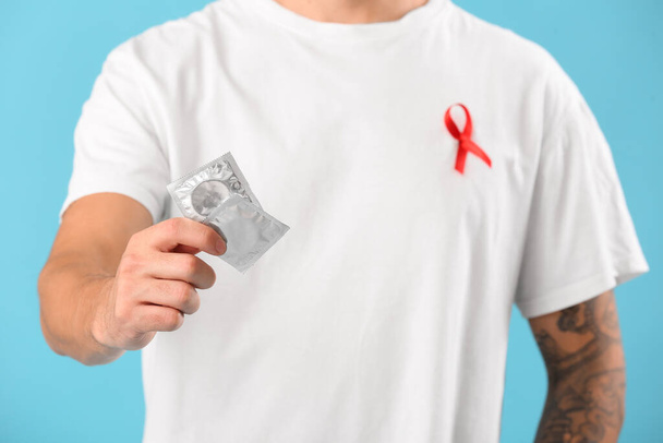 Mladý muž s červenou stuhou a kondomy na modrém pozadí. Koncept Světového dne AIDS - Fotografie, Obrázek