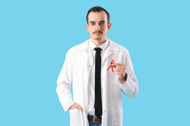 Fiatal férfi orvos piros szalaggal, kék háttérrel. Az AIDS világnapja koncepció - Fotó, kép