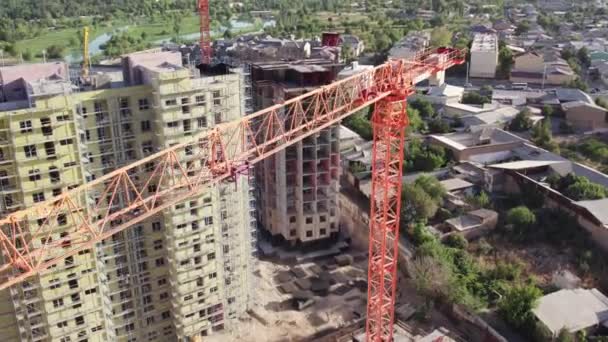 Drone vliegt over bouwkraan tussen flatgebouwen in aanbouw op zomerdag. Luchtzicht. - Video