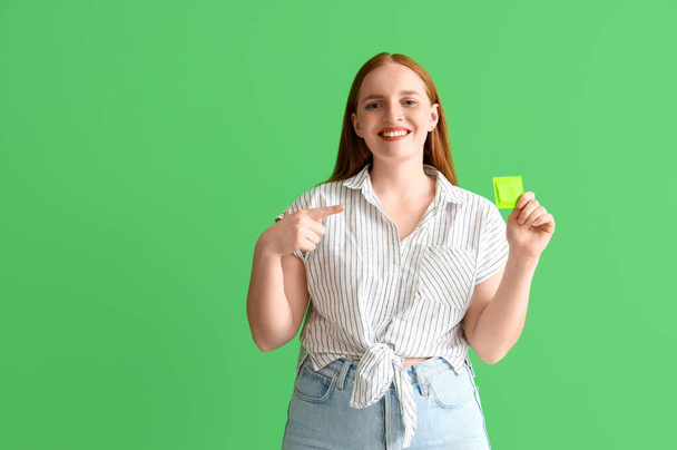 緑の背景にコンドームを指す若い女性 - 写真・画像