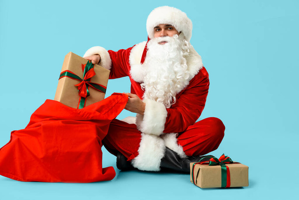 Mavi arka planda duran çanta ve hediye kutularıyla Noel Baba - Fotoğraf, Görsel