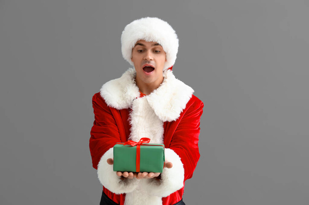 Шокований Санта Клаус з подарунковою коробкою на сірому фоні - Фото, зображення