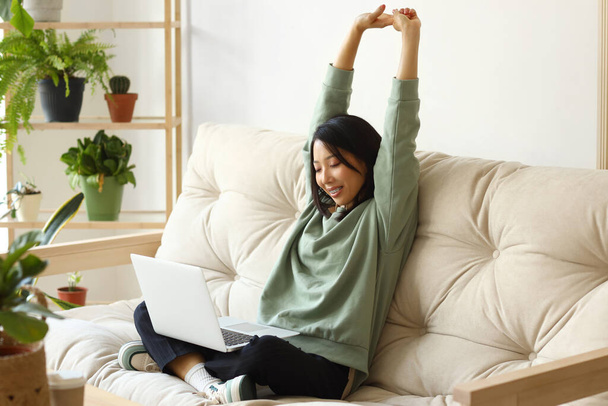 Young Asian woman with laptop stretching at home - Photo, Image