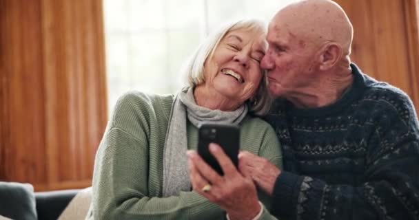 Telefoon, lachen en senior koppel op een bank netwerken op sociale media, mobiele app of het internet. Happy, conversatie en oudere vrouw en man met pensioen scroll op mobiele telefoon samen thuis - Video