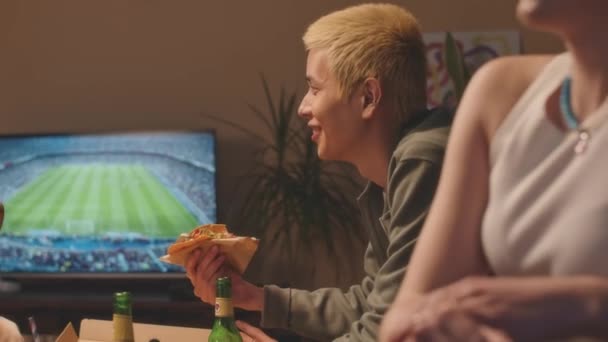 PAN medium shot van diverse vrienden eten fast food en chatten tijdens het zitten door TV in appartement 's nachts - Video