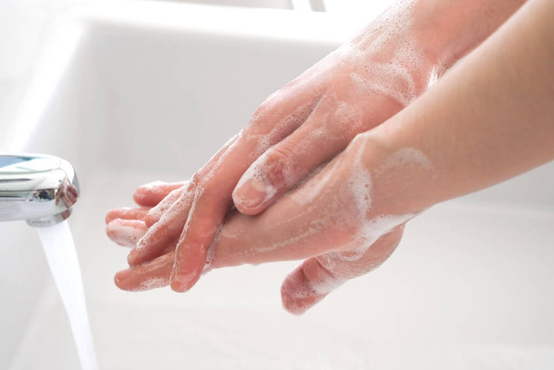 Die Hände einer schönen Frau waschen sich in einem Waschbecken mit Schaum, um die Haut zu waschen und Wasser fließt durch die Hände. Konzept der Gesundheit, Reinigung und Verhinderung des Kontakts von Keimen mit Händen und Schönheit - Foto, Bild