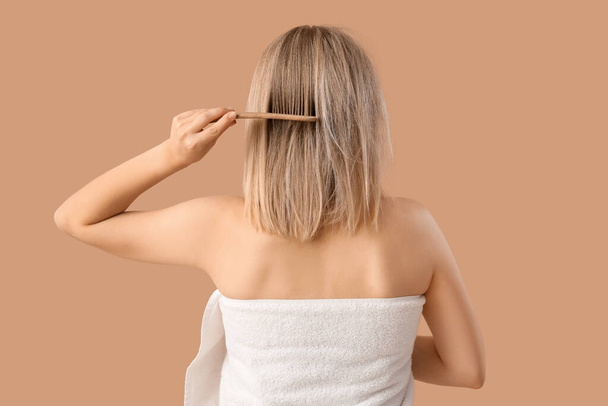 Junge blonde Frau kämmt Haare nach der Dusche auf beigem Hintergrund, Rückseite - Foto, Bild