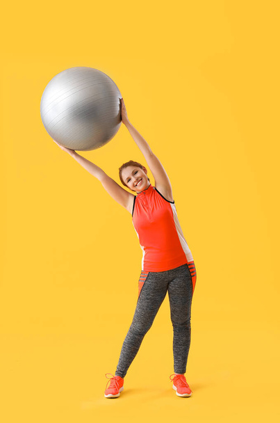 Beautiful young woman in sportswear exercising with fitness ball on yellow background - Zdjęcie, obraz