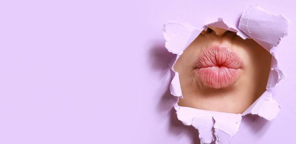 Lips of beautiful young woman visible through torn lilac paper. Banner for design - Photo, Image