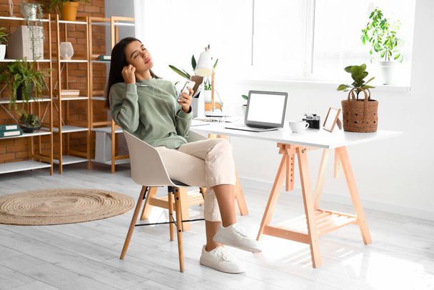 Mujer joven con auriculares y teléfono móvil en la oficina en casa - Foto, Imagen
