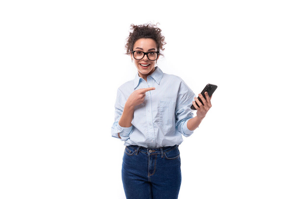 úspěšná brunetka kudrnatý mladý zaměstnanec společnosti žena oblečená v světle modré košili drží telefon v ruce. - Fotografie, Obrázek