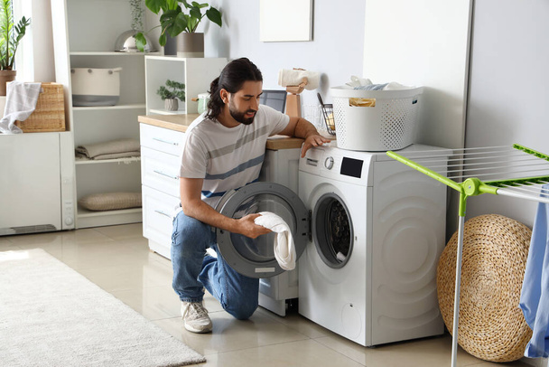 Young man putting laundry into washing machine at home - Fotó, kép