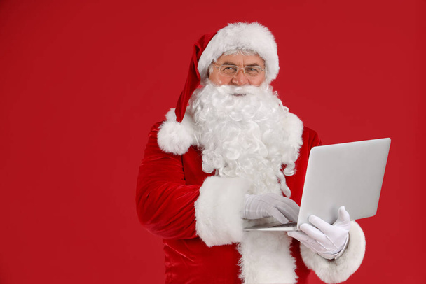 Santa Claus using laptop on red background - Photo, Image