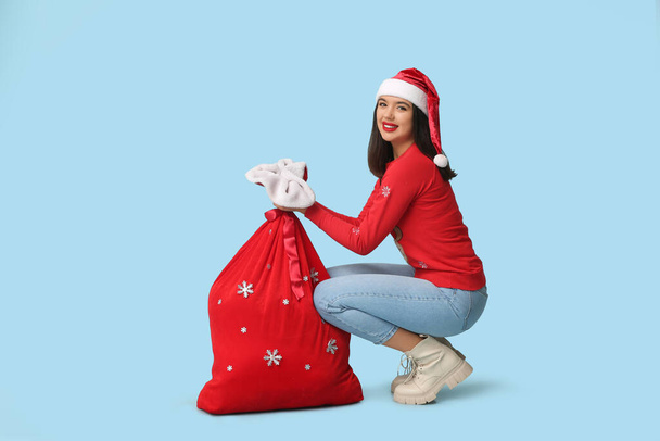 Mavi arka planda bir çanta dolusu Noel hediyesi olan güzel genç bir kadın. - Fotoğraf, Görsel