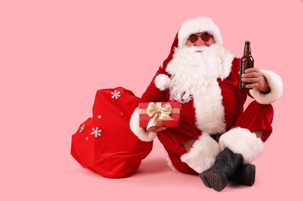 Santa Claus con cerveza y bolsa de regalos sobre fondo rosa - Foto, Imagen