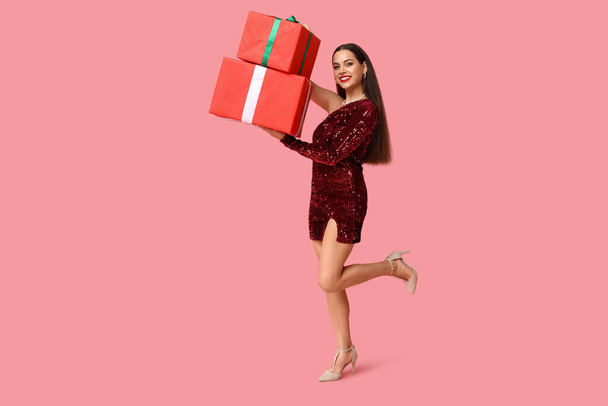 Krásná mladá žena s vánoční dárky na růžovém pozadí - Fotografie, Obrázek