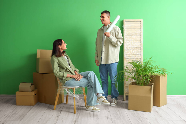 Felice giovane coppia con involucro elasticizzato e scatole in movimento vicino alla parete verde - Foto, immagini