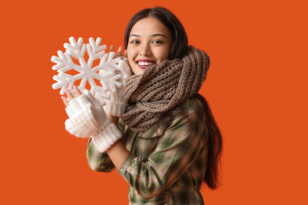 Красивая молодая азиатка в теплом шарфе со снежинкой на оранжевом фоне - Фото, изображение