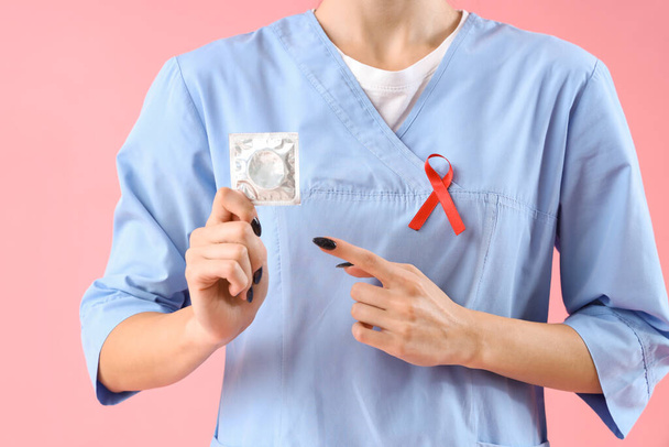 Kobieta lekarz z czerwoną wstążką i prezerwatywą na różowym tle. Koncepcja Światowego Dnia AIDS - Zdjęcie, obraz