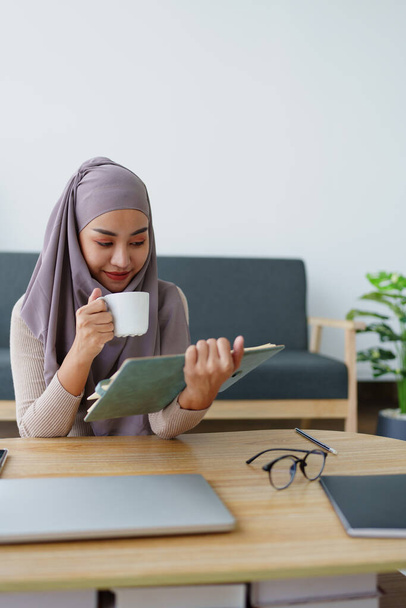 Muslim undergraduate student drinks coffee while read studying at home - Photo, Image