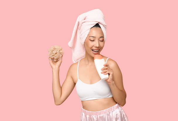 Joven mujer asiática con gel de ducha y esponja sobre fondo rosa - Foto, imagen