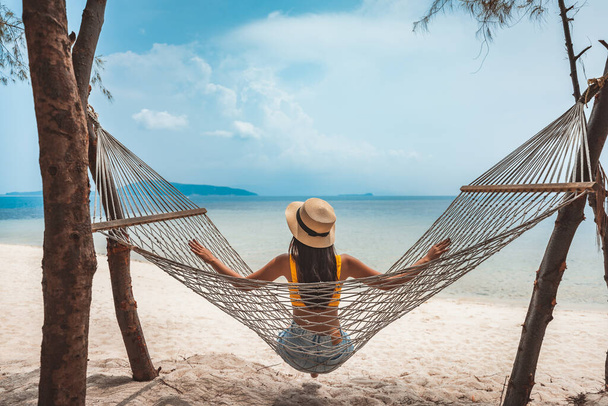 Summer travel vacation concept, Happy traveler Asian woman with hat relax in hammock on beach in Koh Rap, Samui, Surat Thani, Thaiföld - Fotó, kép