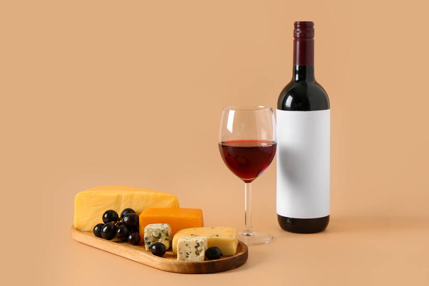 Holztafel mit leckerem Käse, Trauben, Flasche und Glas Wein auf beigem Hintergrund - Foto, Bild
