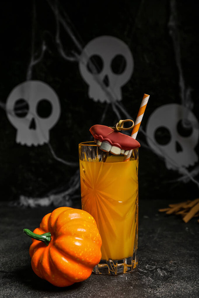 Copo de delicioso coquetel de laranja para Halloween com dentes e abóbora no fundo escuro, close-up - Foto, Imagem