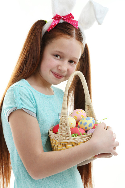 Beautiful little girl wearing Easter bunny ears and holding wicker basket with Easter eggs, isolated on white - 写真・画像
