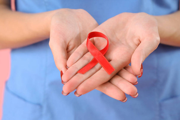 ピンクのバックグラウンドに赤いリボンを持つ女性医師,クローズアップ. 世界エイズデーコンセプト - 写真・画像