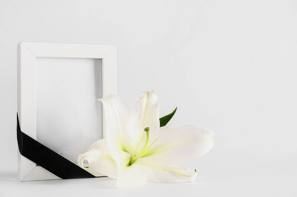 Valkoinen lilja ja valokuvakehys, jossa musta nauha valkoisella taustalla - Valokuva, kuva