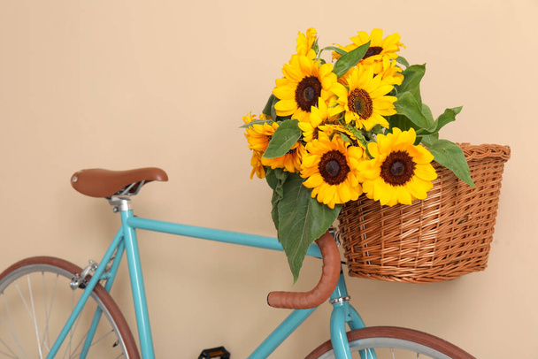 Bicicleta con ramo de hermosos girasoles en canasta de mimbre cerca de la pared beige - Foto, imagen