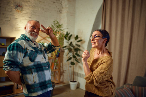 Adorable mature couple dancing of happiness, joyful while listening music and relax at home. Keep moving. Concept of love, retirement life, active lifestyle, fun, pensioners, cozy, winter holidays. - Photo, Image