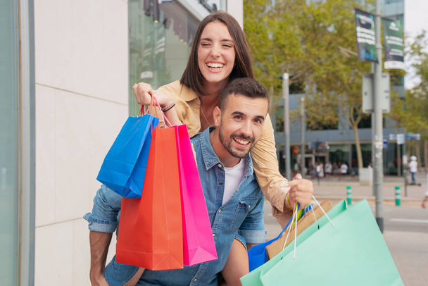 幸せな白人男性は,興奮,週末,家族のショッピングバッグを持って一緒に楽しんでいる彼のガールフレンドを背中に運ぶ. - 写真・画像