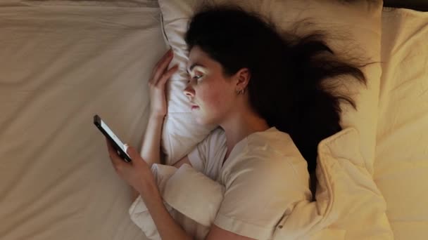Slaap tijd. Bovenaanzicht van blanke jonge vrouw met behulp van smartphone in bed. Begrip slapeloosheid en verslaving aan sociale media - Video