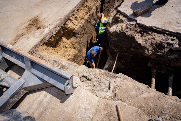 Herramienta de excavadora pequeña, hoja de excavadora inferior delantera, excavadora estacionada con tren de aterrizaje de goma está de pie junto a la trinchera en el sitio de construcción. - Foto, Imagen