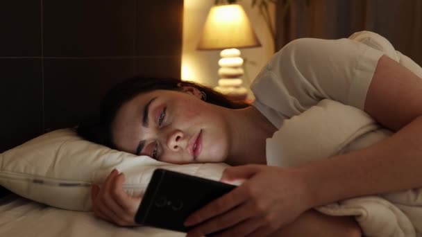 Uneton ihminen. Niin. Lähikuva muotokuva valkoihoinen nainen käyttää puhelinta makaa sängyssä. Unettomuuden ja sosiaalisen median riippuvuuden käsite. - Materiaali, video