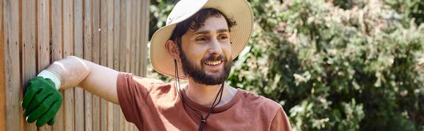 handsome and bearded farmer in sun hat standing near fence in countryside, rural lifestyle banner - Photo, Image